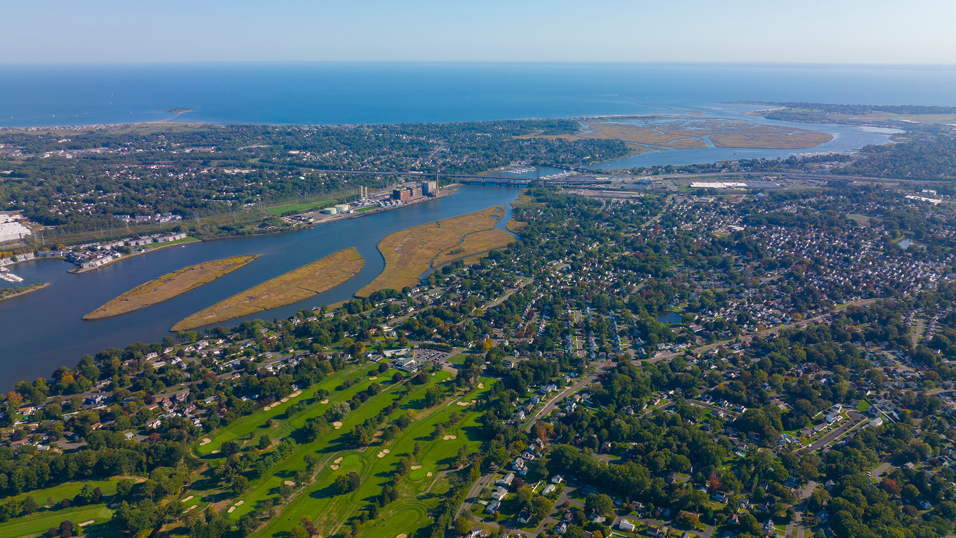 Aerial view of a town with a river surrounded by land and water, under a clear sky.