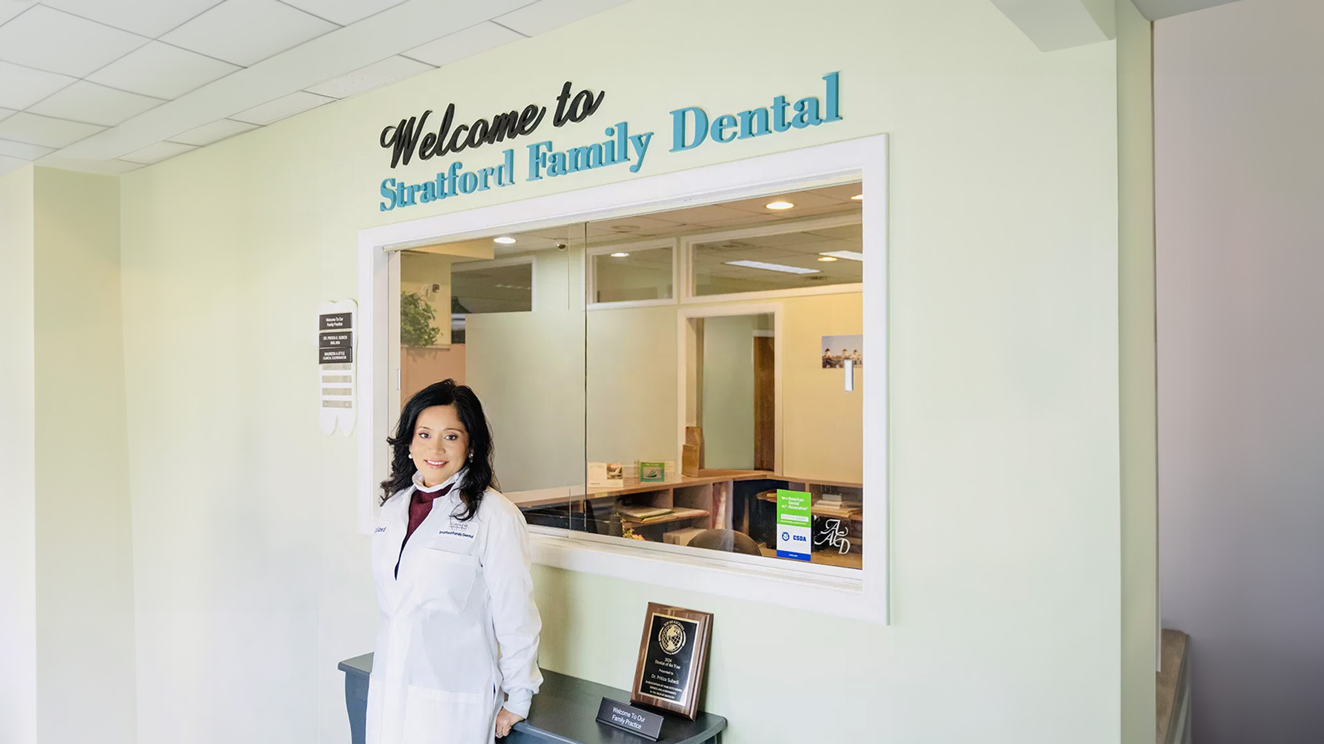 The image displays a person standing in front of a sign reading  Welcome to Stratford Family Dental  with a background that includes a reception area and a waiting room.
