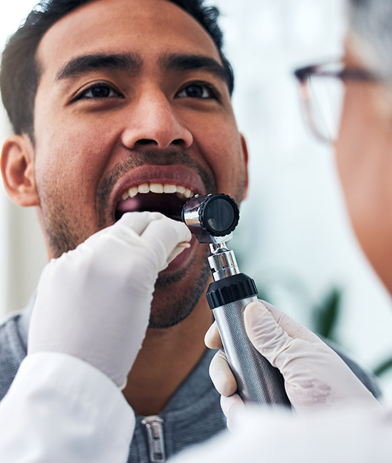 A man receiving dental care with an oral device placed in his mouth by a dentist.