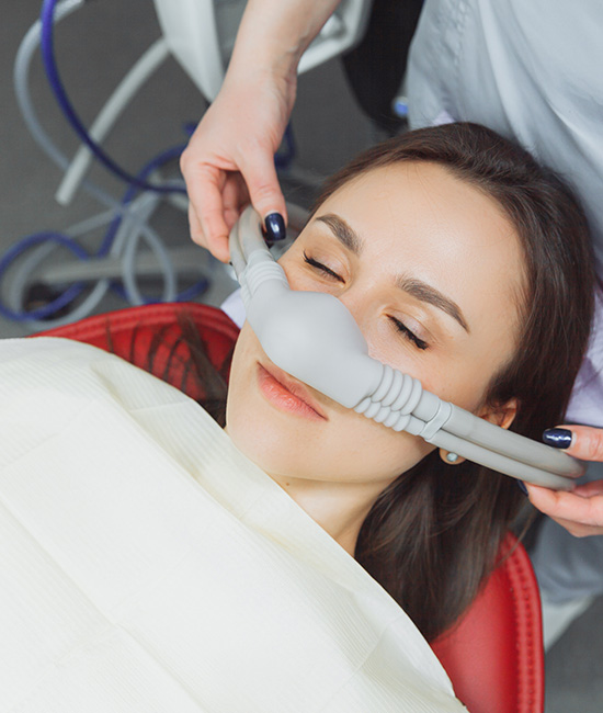 The image shows a woman lying on a dental chair with her eyes closed, receiving dental treatment. She appears relaxed, and there s a dental hygienist working on her mouth using an air spray device.