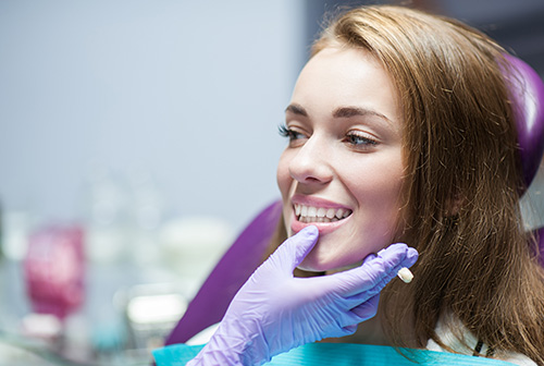 A woman sitting in a dental chair with a smile on her face, receiving dental care from a professional.