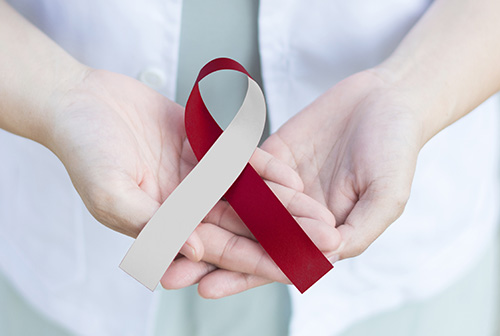 The image shows a pair of hands holding a ribbon with a cancer awareness symbol, suggesting support for cancer awareness or fundraising.