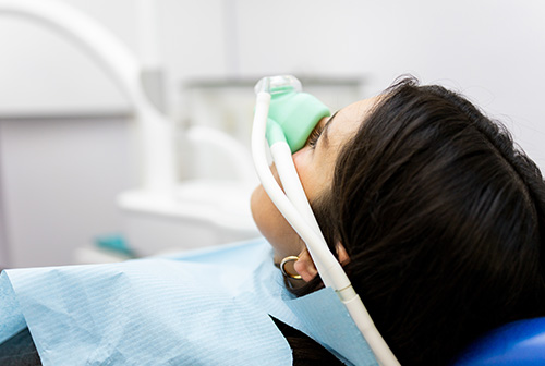 The image shows a person lying down with an oxygen mask on their face, likely in a medical setting such as a hospital or dental clinic.