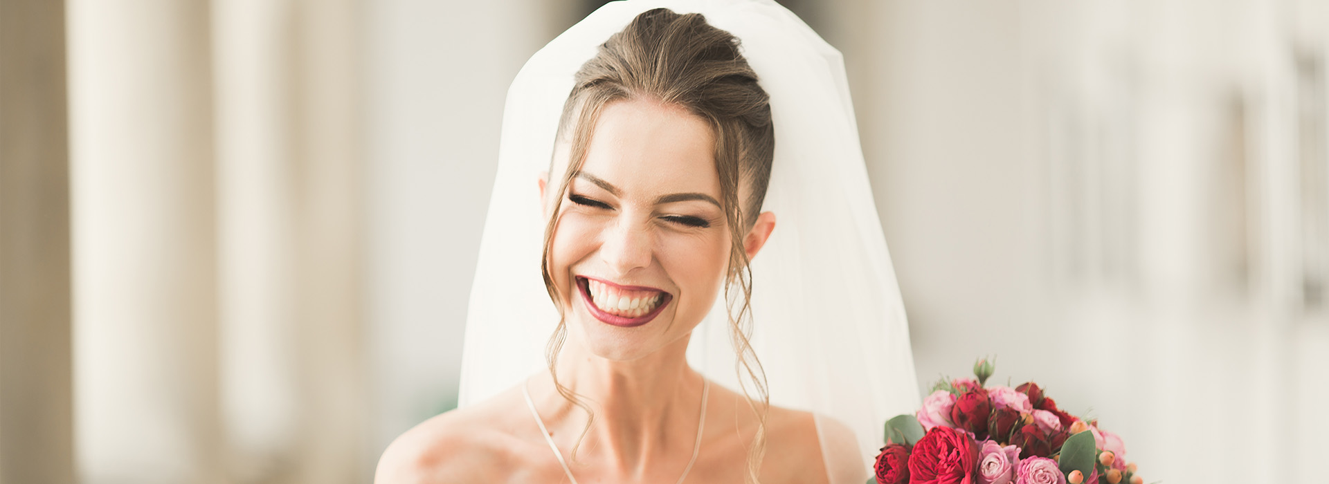 A smiling bride holding a bouquet of flowers with a veil over her face.