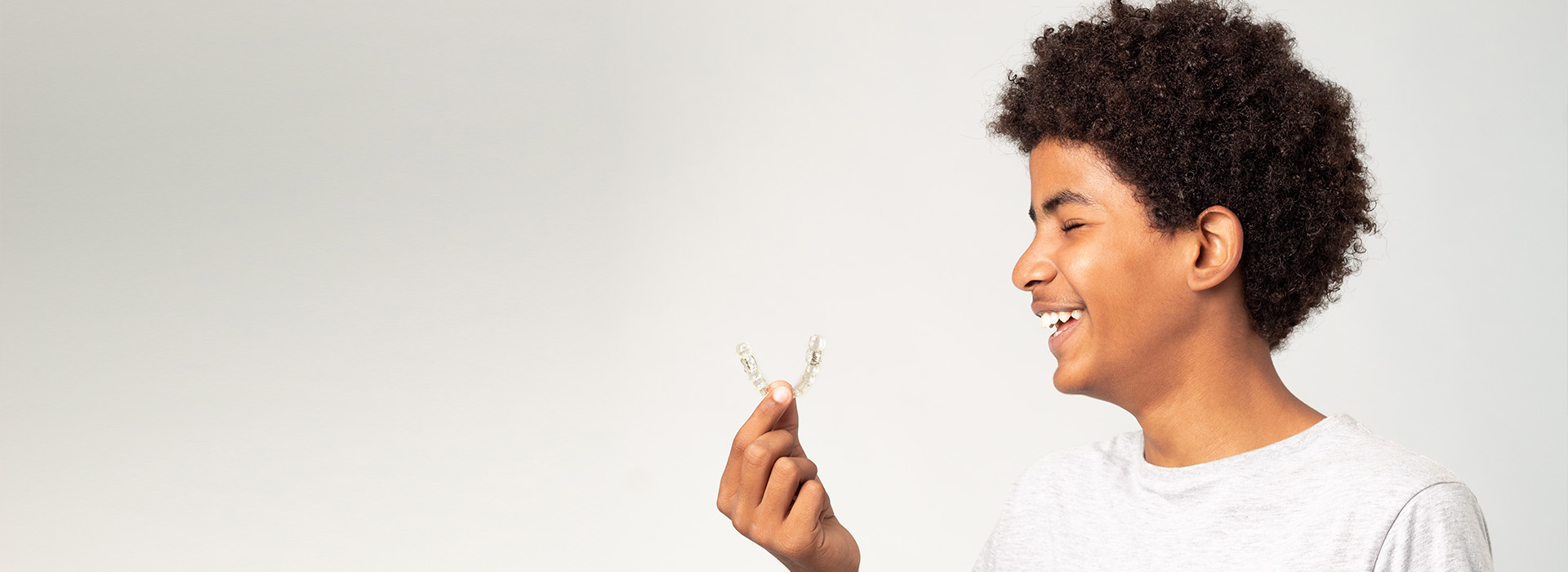 A young man with curly hair holds a small bird in his hand, smiling against a white background.