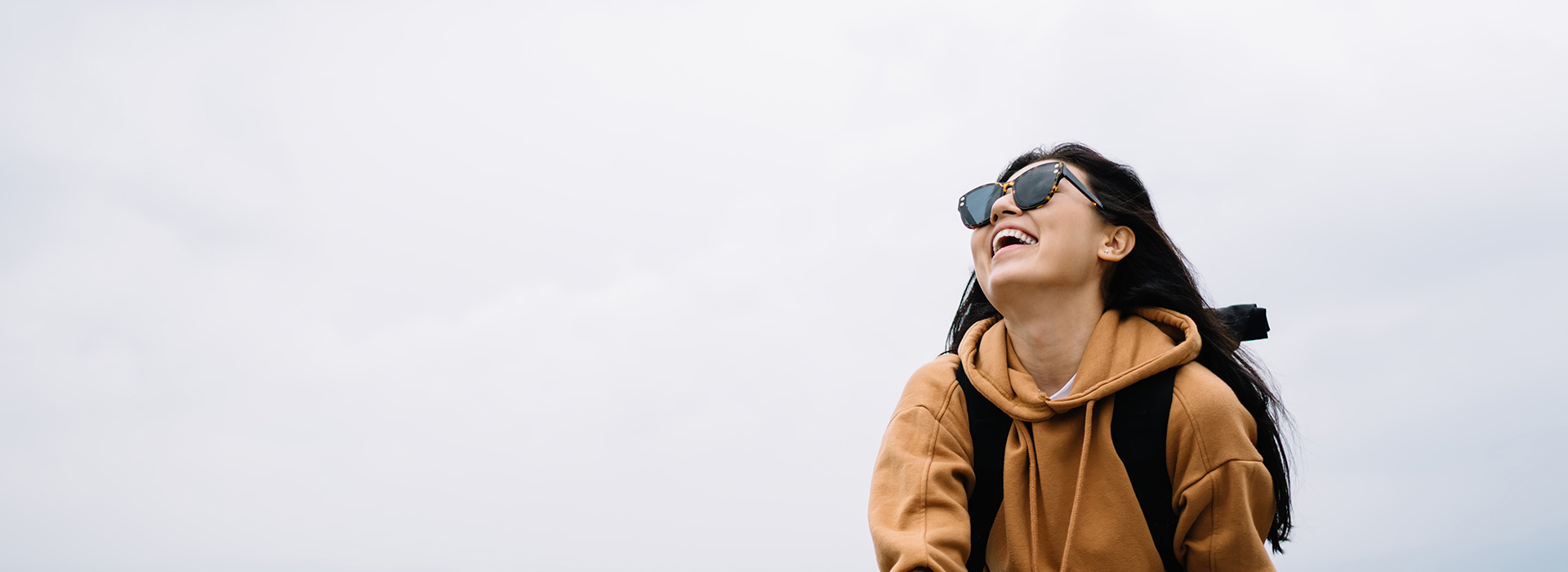 A person is standing outdoors on a clear day, wearing a backpack and sunglasses, with a bright sky above them.