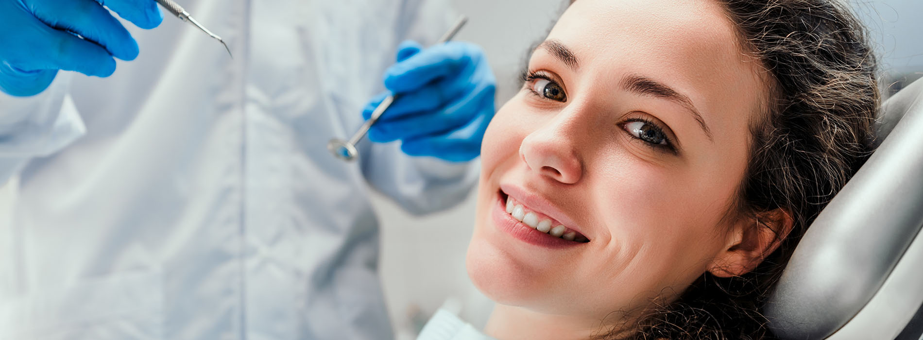 The image shows a smiling woman wearing blue gloves with a medical mask on her face, sitting in front of a table with various medical equipment, including microscopes and test tubes.