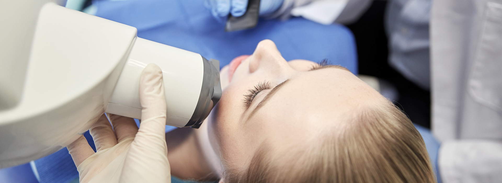 The image shows a person receiving a medical treatment with a device attached to their face, possibly in a healthcare setting, with visible medical equipment and personnel in the background.