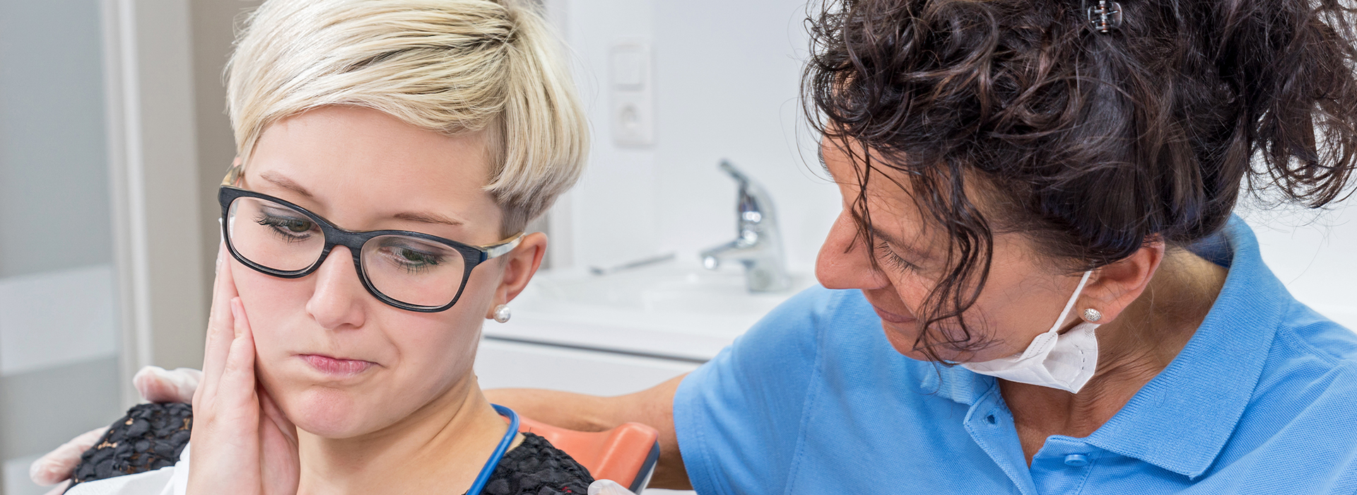 The image shows a woman performing an eye examination on a young adult with glasses, who appears to be seated at a dental chair.