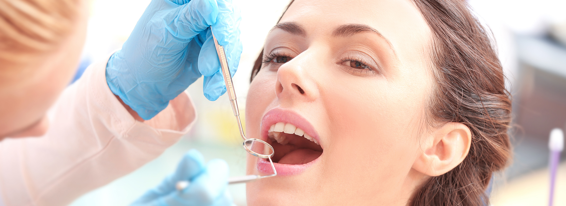 A woman receiving dental care with a syringe in her mouth, surrounded by dental professionals wearing gloves and blue scrubs.