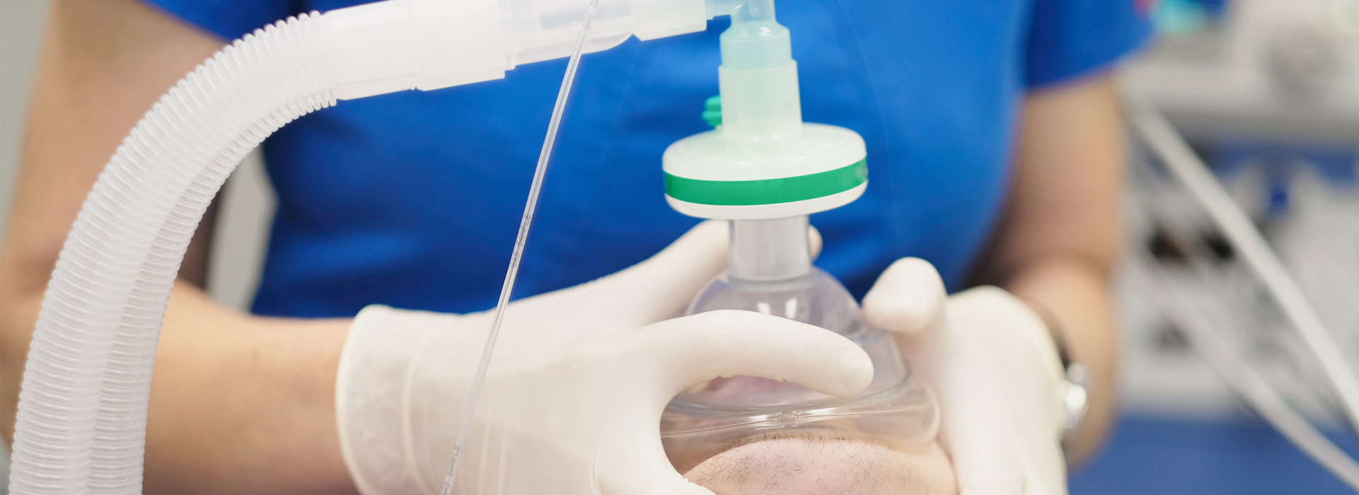 The image shows a person wearing medical gloves and a mask, holding a syringe with a clear liquid inside, which appears to be a medication bottle. The setting suggests a medical environment, possibly a hospital or clinic.
