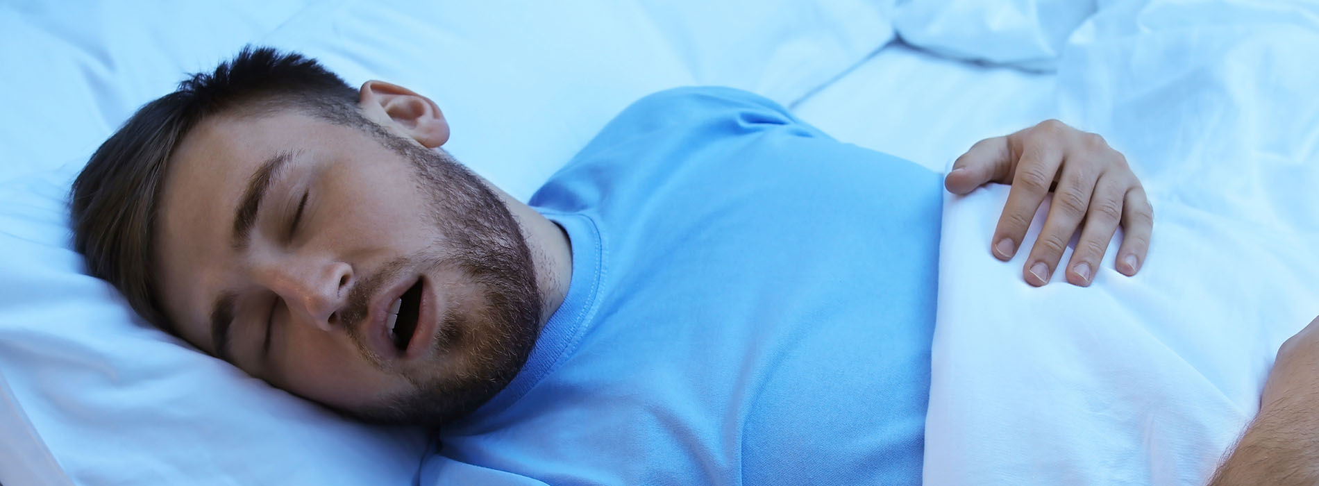 The image shows a man lying on his side on a bed with his eyes closed, appearing to be asleep or resting.